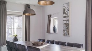A dining area with a long wooden table, six chairs, and pendant lighting.
