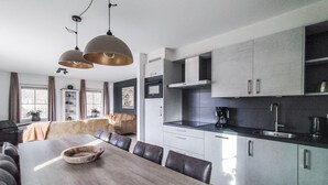 A modern kitchen with a large island, dark countertops, and stainless steel appliances. There is a dining area with a wooden table and leather chairs.