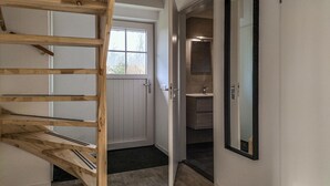 A wooden staircase leading to a white door, a bathroom with a sink and mirror, and a view of the outside through a window.