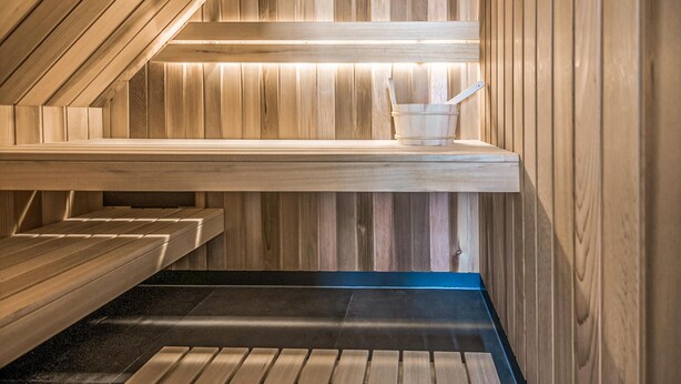 A sauna with wooden walls and benches, a bench with a bucket, and a blue mat on the floor.
