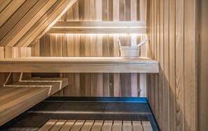 Un sauna avec des murs et des bancs en bois, un banc avec un seau, et un tapis bleu sur le sol.
