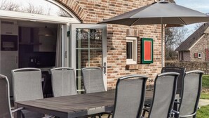 An outdoor patio with a table and chairs, a large umbrella, and a brick building with a window and a picture frame.