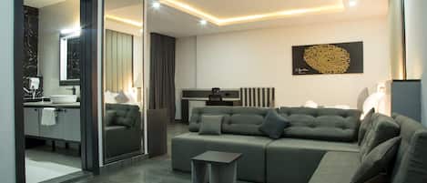 A modern living room with a grey sofa, a small side table, and a kitchen area visible through an open door.