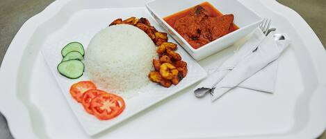 A tray with white rice, sliced tomatoes, cucumber slices, fried plantains, and a bowl of red curry.