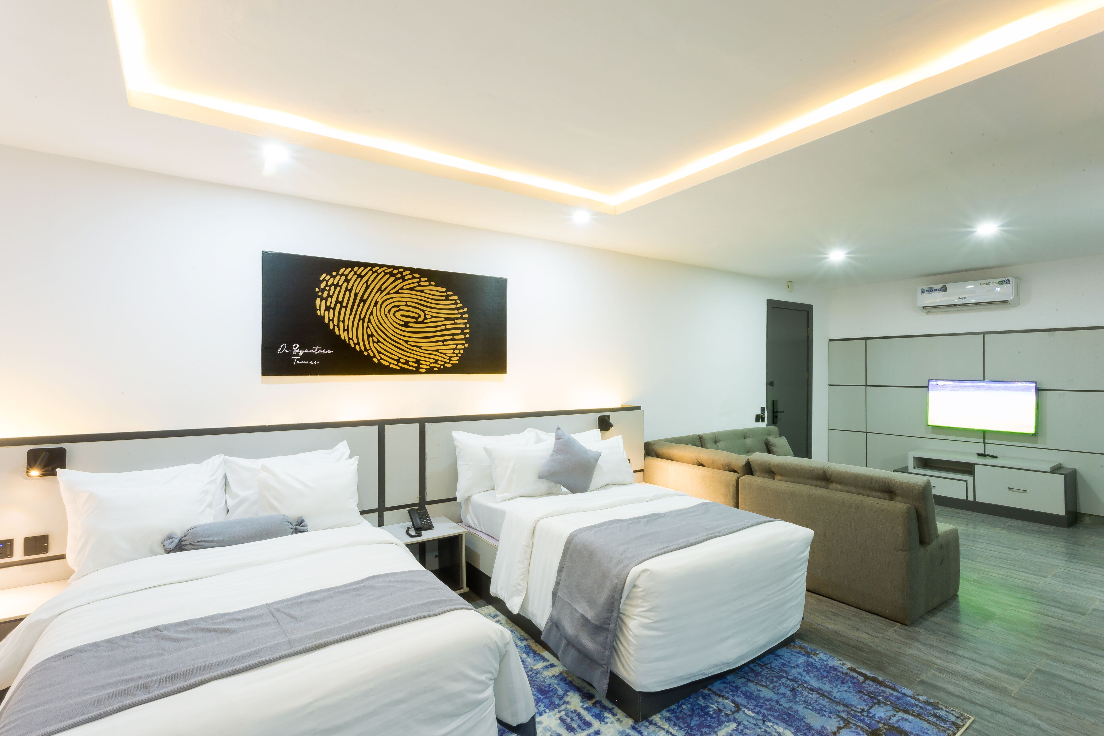 A hotel room with two beds, a sofa, a TV, and a large artwork on the wall.