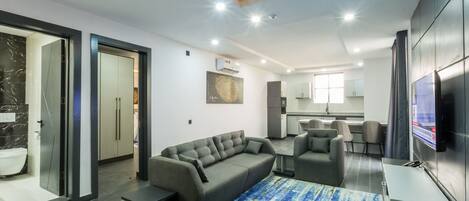 A modern living room with a grey sofa, a blue rug, and a flat-screen TV mounted on the wall.