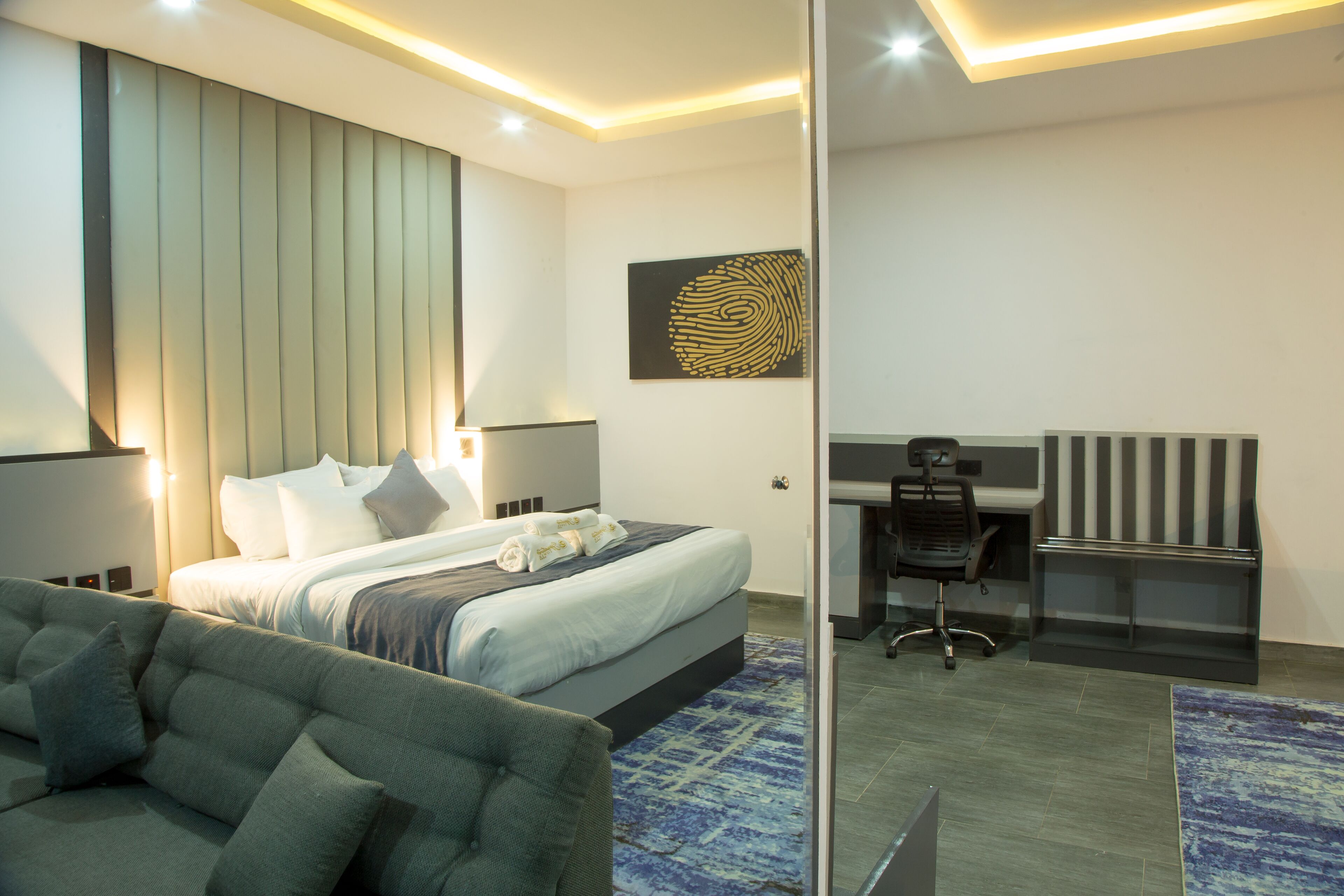 A modern hotel room with a large bed, a desk, and a sofa.