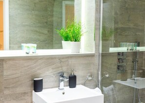 A modern bathroom with a white sink, a mirror, a potted plant, and a glass shower enclosure.