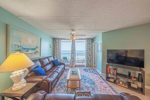 A living room with a sofa, a coffee table, a TV, and a bookshelf. - Oceanfront condo at Southpoint unit 606 (Ponce Inlet)