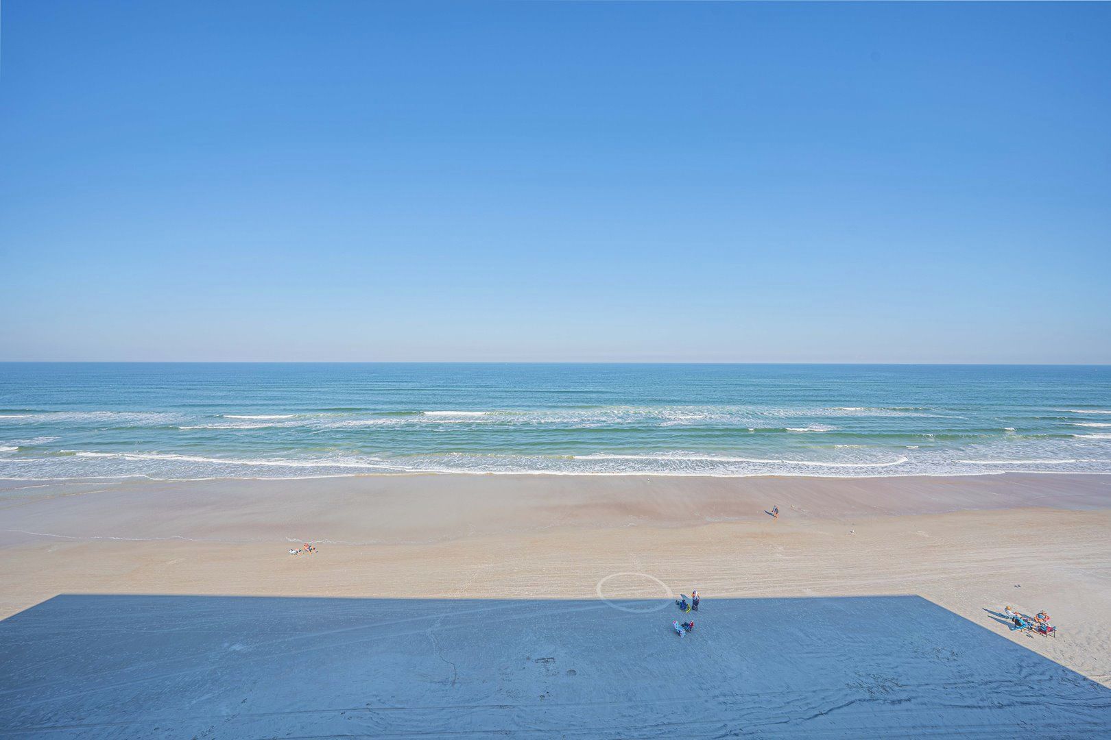 A beach with a clear sky and calm sea. There are people and beach chairs on the sand.