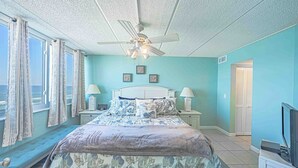 Ein Schlafzimmer mit Bett, Nachttischen, Deckenventilator und Meerblick.