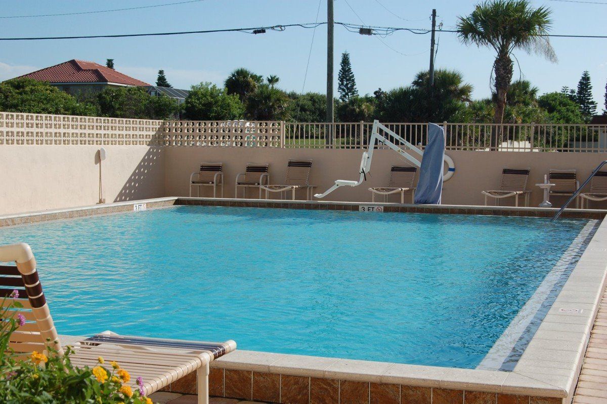 Una piscina rectangular con superficie de agua azul cristalina, rodeada por una solana con baldosas y una cerca blanca.
