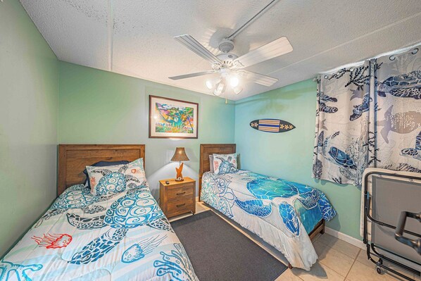 A room with two beds, a ceiling fan, a framed picture, and a surfboard decoration.