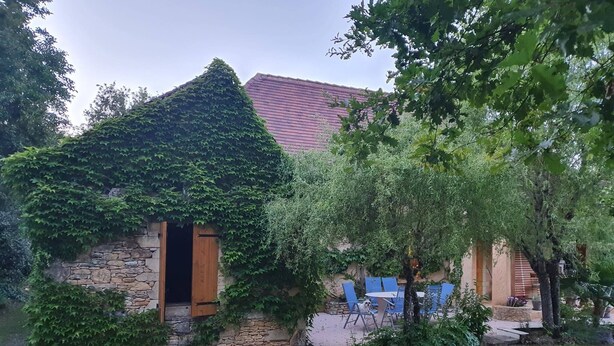 A stone house with a red roof, ivy-covered walls, and a small porch with blue chairs. - Maison de Vacances au Calme , à 5 Minutes de la Capitale de la Préhistoire ! (Tursac)