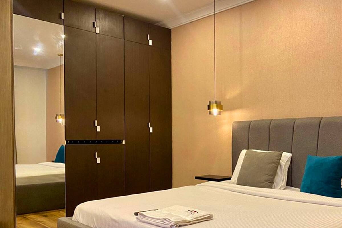A modern bedroom with a large bed, a wardrobe, and a nightstand.