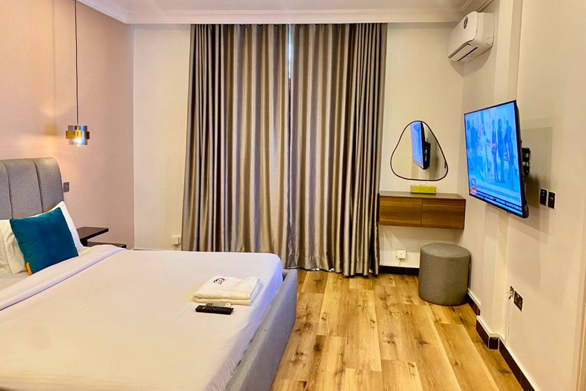 A modern hotel room with a bed, a desk, a television, and an air conditioning unit.