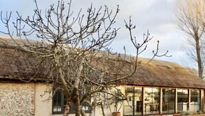 A building with a thatched roof, a stone wall, and a glass extension. - Poplars Farm Barns, Brand new stunning thatched barn conversion (Chichester)