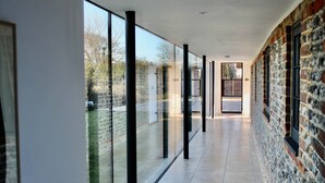 A corridor with glass walls, a stone wall, and a tiled floor. - Poplars Farm Barns, Brand new stunning thatched barn conversion (Chichester)