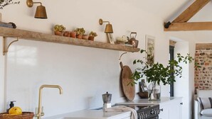 A kitchen with white cabinetry, a black stove, and wooden beams on the ceiling. - Poplars Farm Barns, Brand new stunning thatched barn conversion (Chichester)
