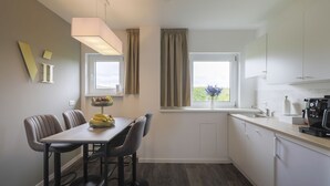 A modern kitchen with a dining area, featuring a table with chairs, a window with curtains, and a coffee machine. - VIU2 Hannover (Hannover)