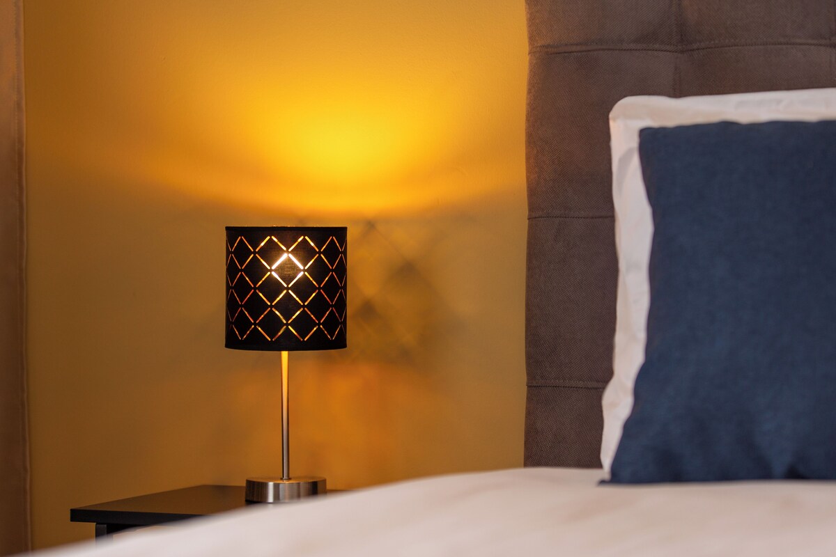 A bed with a blue pillow, a nightstand with a lamp, and a brown headboard.