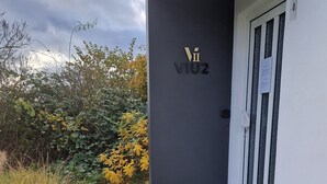 A modern building entrance with a dark facade, a door with a window, and a sign with 'VI02' on it. - VIU2 Hannover (Hannover)