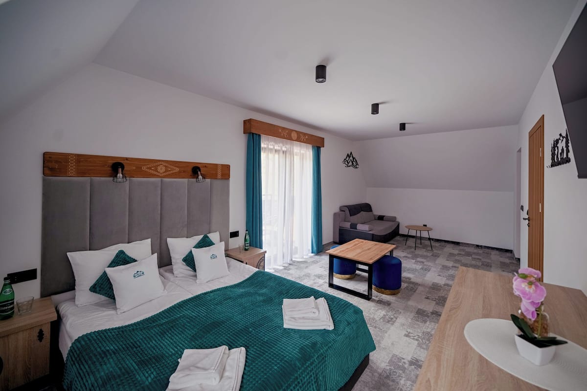 A modern hotel room with a large bed, a desk, a sofa, and a small table.