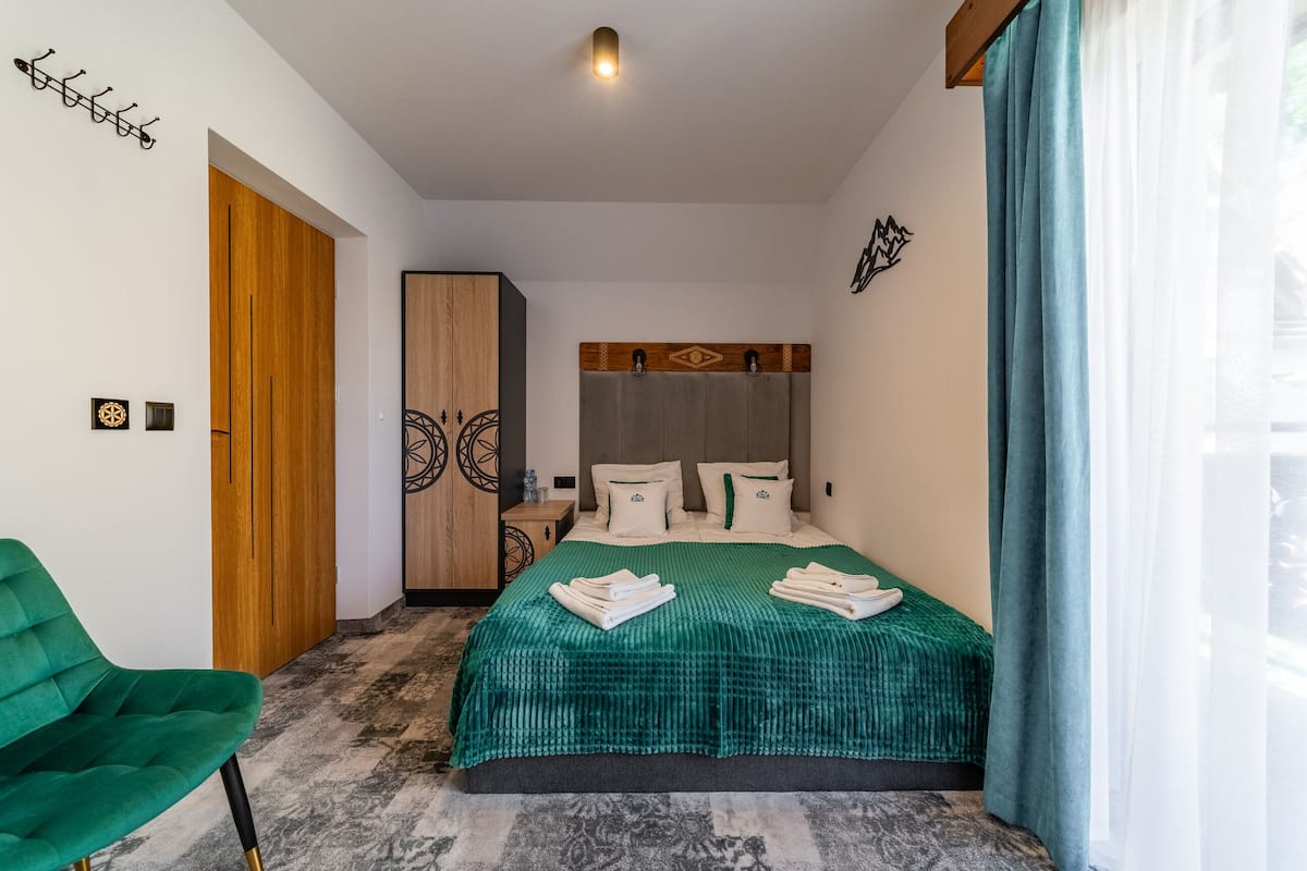 A modern hotel room with a large bed, a green chair, and a wooden wardrobe.