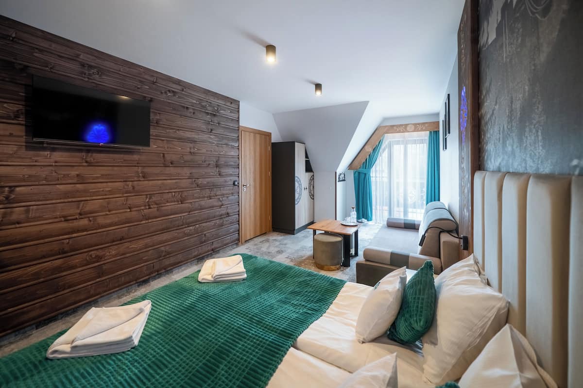 A modern room with a wooden wall, a flat-screen TV, a green rug, a sofa, and a window with curtains.