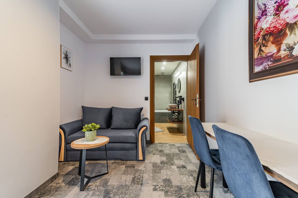 A modern living room with a grey sofa, a small round table, and a TV mounted on the wall.