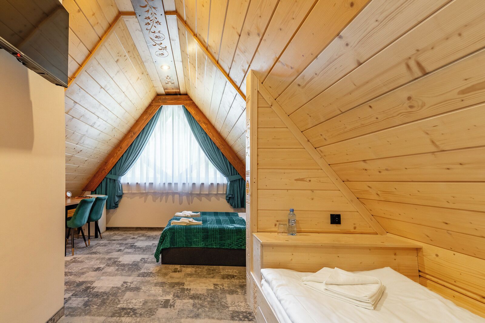 A cozy attic bedroom with a sloped ceiling, a bed, a desk, and a chair.