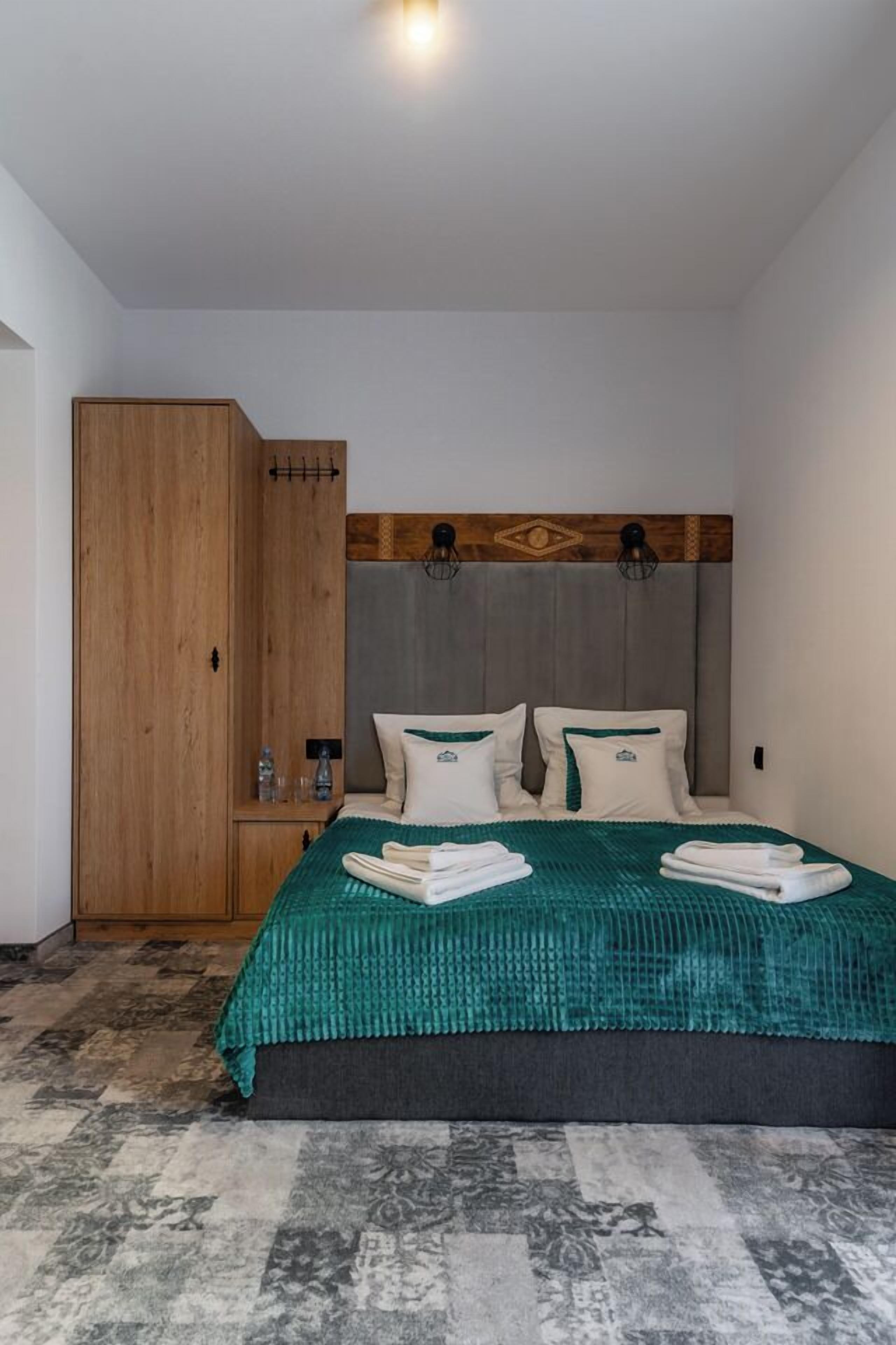 A bedroom with a bed, a wooden wardrobe, and a headboard with wall-mounted lights.