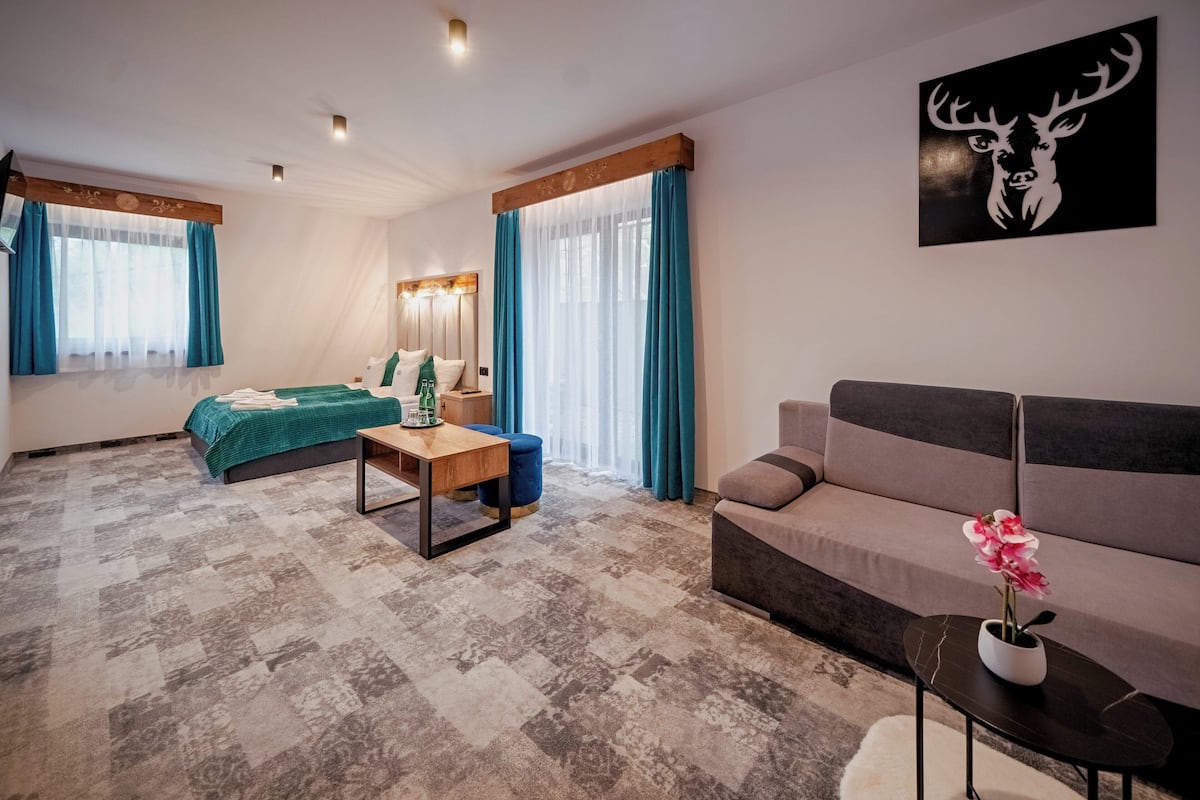 A modern hotel room with a bed, a sofa, a small table, and a decorative wall piece.
