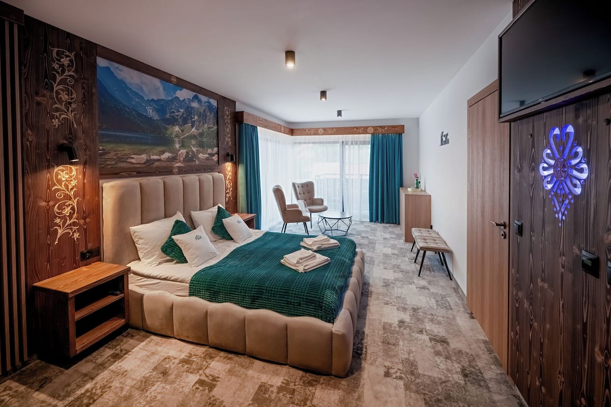 A bedroom with a large bed, a wooden wardrobe, a TV, and a painting of mountains.