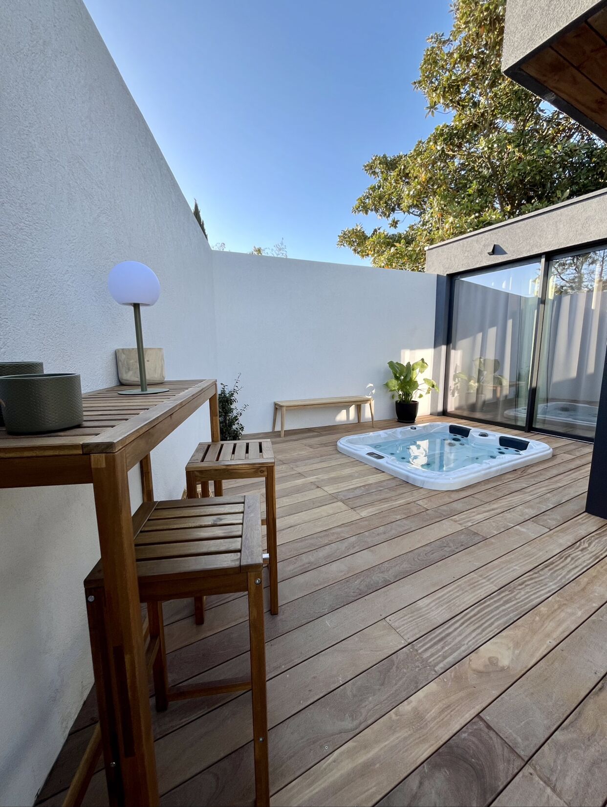 Een houten terras met een jacuzzi, een tafel en stoelen.