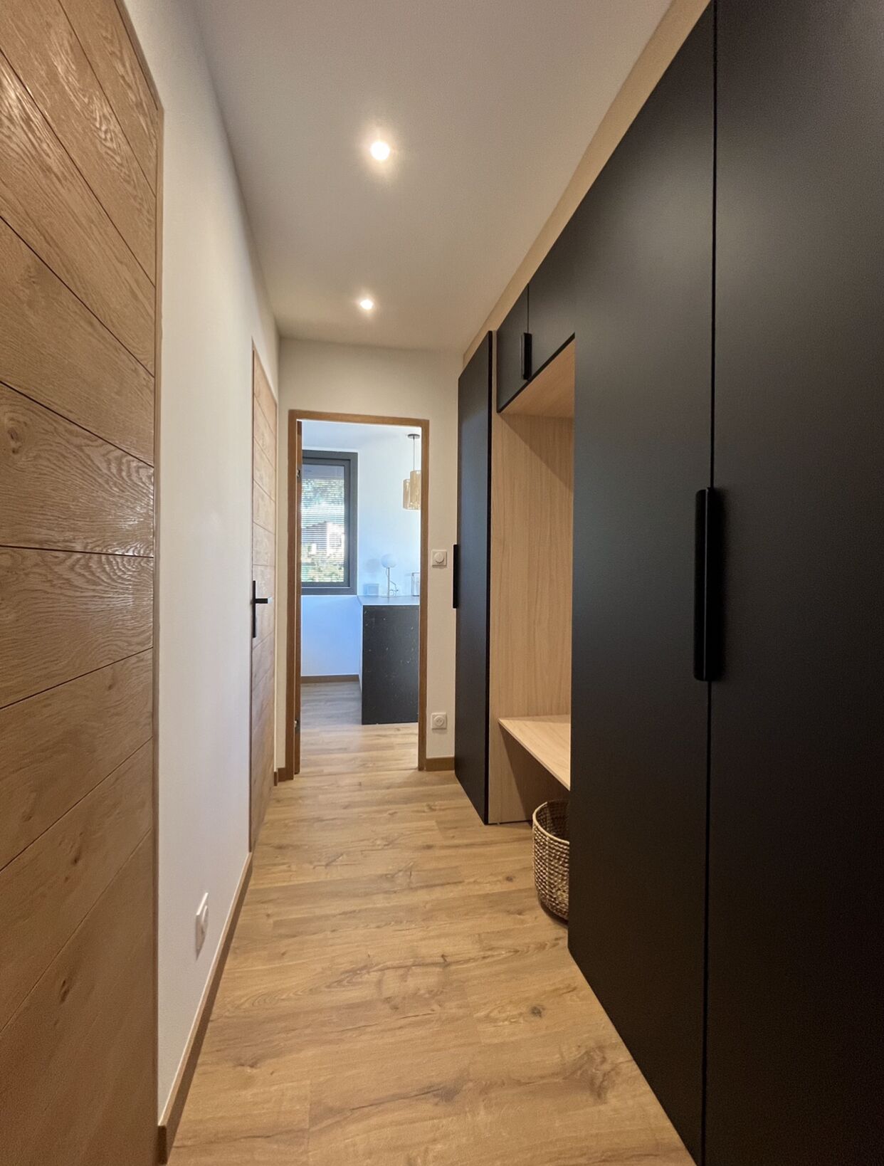 A narrow hallway with wooden paneling on one side and a dark wardrobe on the other.