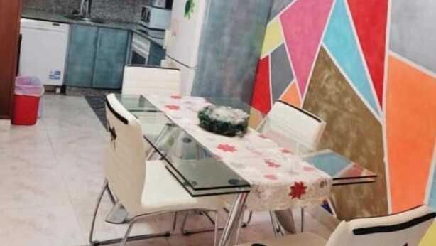 A dining area with a glass table, white chairs, and a colorful geometric wall design. - Apartamento Prémium en la Familia Vigo (Vigo)
