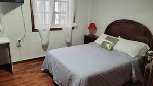A bedroom with a wooden floor, a bed with grey bedding, a nightstand with a lamp, and a TV mounted on the wall. - Apartamento Prémium en la Familia Vigo (Vigo)