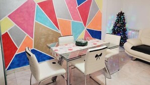 A dining area with a glass table and chairs, a colorful geometric wall, and a Christmas tree in the background. - Apartamento Prémium en la Familia Vigo (Vigo)