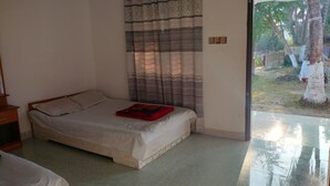 Un dormitorio con cama, mesita de noche, ventana con cortinas y vistas a un espacio exterior con árboles y una valla.