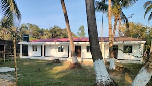 Una casa de un piso con techo rojo, rodeada de césped y palmeras.