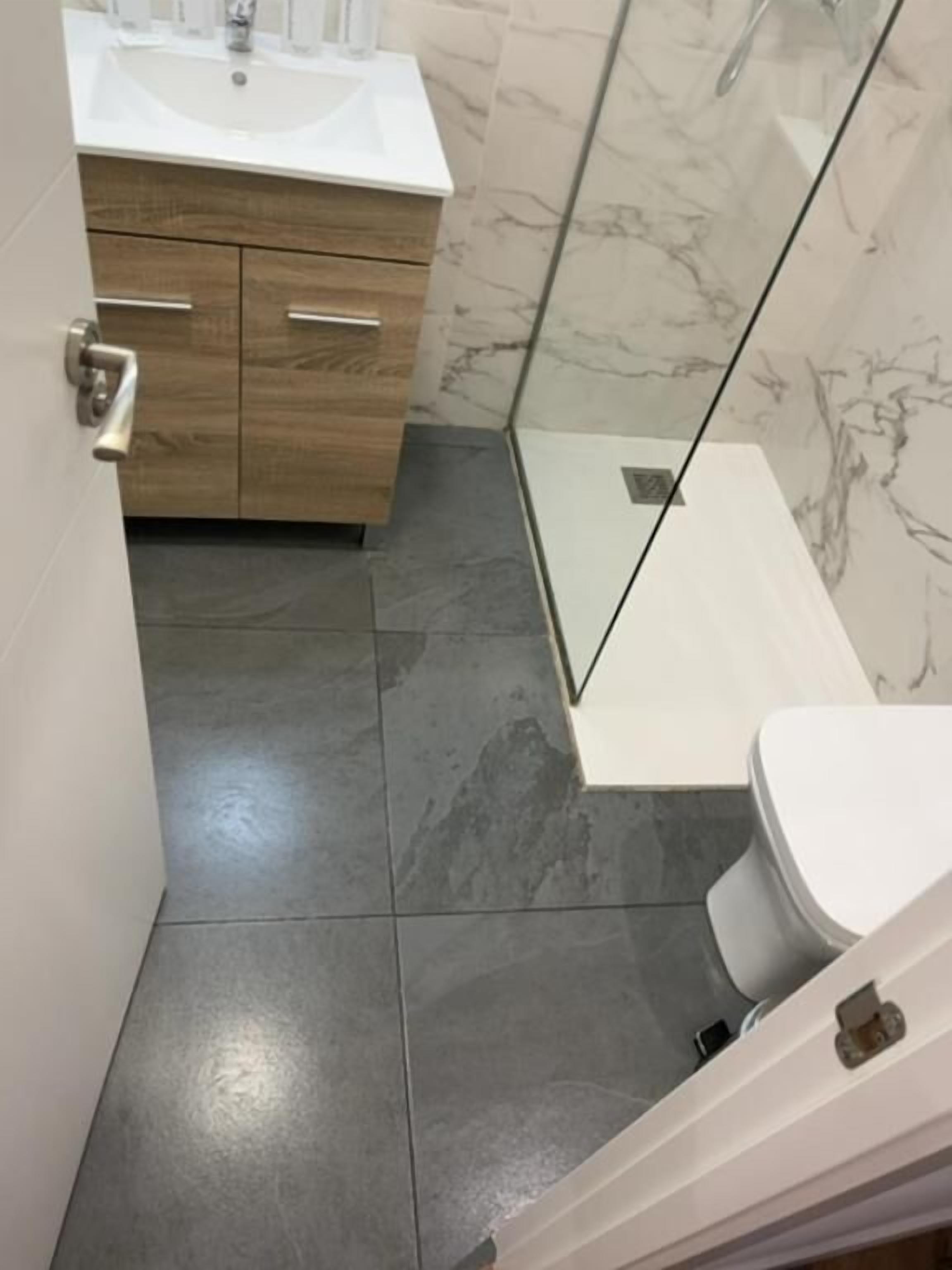 A modern bathroom with a white sink, wooden vanity, and a glass shower enclosure.