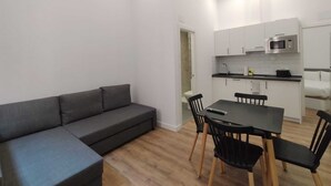 A compact living space with a sofa, dining table, chairs, and a kitchenette. - Apartamentos Vacceas by gaiarooms (Salamanca)