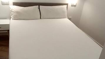 A neatly made bed with white linens and a wooden headboard. There are two bedside tables with lamps on either side of the bed.