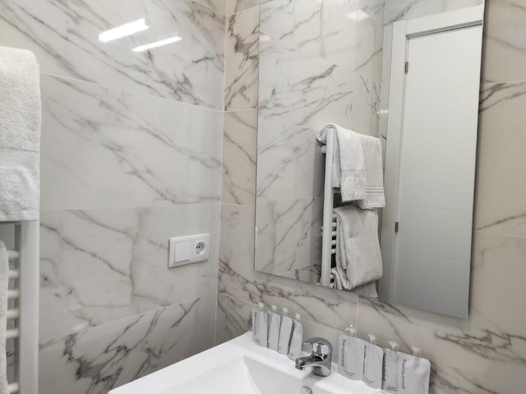 Un baño con paredes de mármol, un lavamanos blanco y un perchero para toallas.