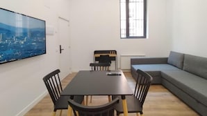 A modern living room with a dining area, featuring a large flat-screen TV, a gray sofa, and a dining table with chairs. - Apartamentos Vacceas by gaiarooms (Salamanca)