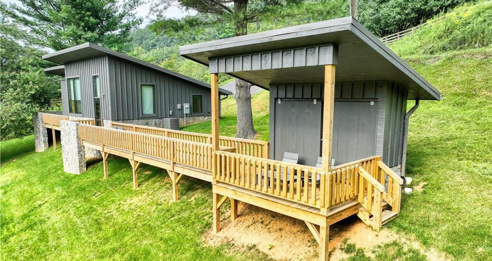 Eine moderne Holzhütte mit einer hölzernen Terrasse, die zwei Gebäude verbindet, umgeben von üppigem Grün.