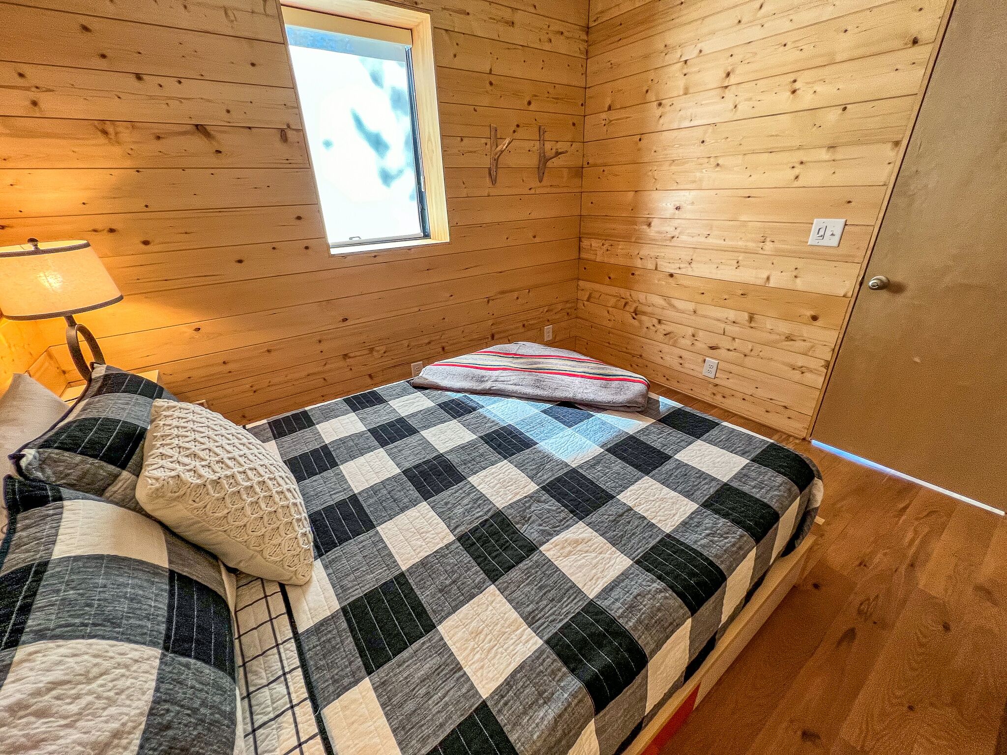 A cozy room with a checkered bedspread, a lamp, and a window with a view.
