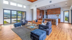 Uma sala de estar ampla com uma grande porta de vidro deslizante que dá para uma varanda, uma cozinha com armários de madeira e uma ilha central, e uma área de estar com sofás e uma mesa de centro.