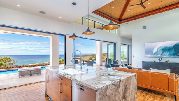 Uma cozinha moderna com uma ilha grande, uma sala de jantar com vista para o oceano e uma sala de estar com uma TV grande.
